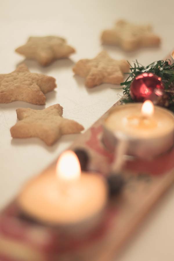Kerzen auf einem selbstgebastelten Adventskranz, dazu sternenförmige Kekse im Hintergrund